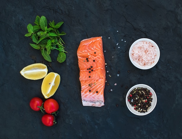 Ingredientes Filete de salmón crudo, limón, tomates cherry, menta fresca y especias sobre fondo de piedra oscura