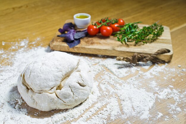 Foto ingredientes para focaccia: masa, tomates, romero, tomillo, albahaca, aceite de oliva en una mesa de madera.