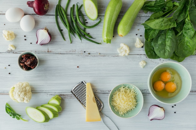 Ingredientes para hacer comida vegana saludable. Coliflor, calabacín, cebolla morada, judías verdes, huevos, queso y hojas de espinaca para hacer frittata de verduras