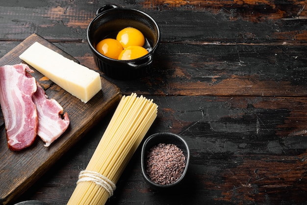 Ingredientes para hacer pasta alla carbonara prosciutto, pasta cruda, sobre la vieja mesa de madera oscura.