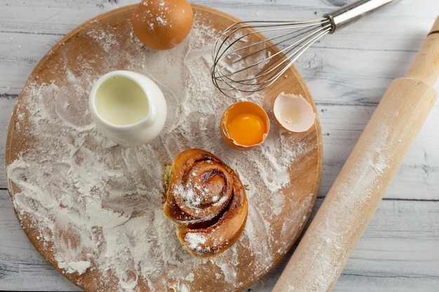 Los ingredientes para hacer productos horneados en la mesa son harina de trigo, huevos, leche, así como un rodillo y una tabla de madera.