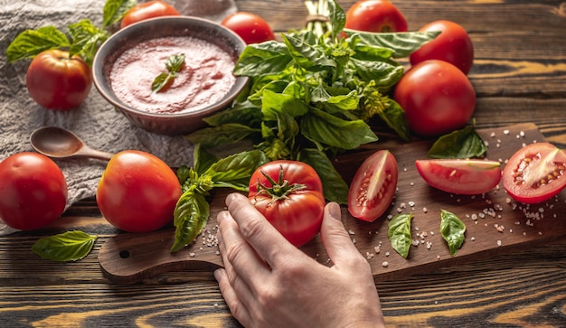 Ingredientes para hacer salsa de tomate y albahaca un bol con salsa fresca y manos sosteniendo un tomate casero maduro
