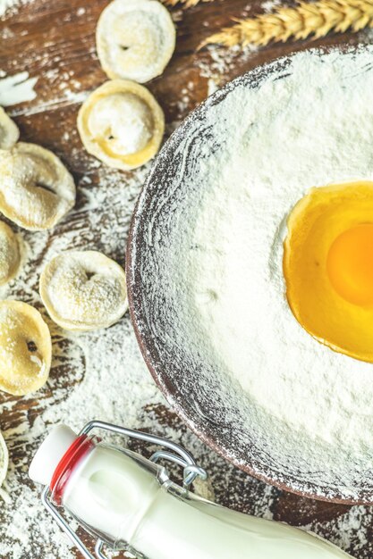 Ingredientes y herramientas para hornear huevos de harina y vaso de leche y albóndigas de raviolis italianos tradicionales deliciosos caseros crudos en el fondo de la mesa rústica de madera enfoque selectivo