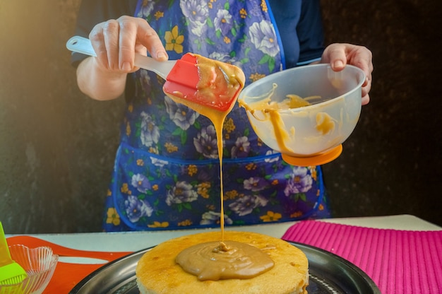 Ingredientes para hornear y utensilios para cocinar bizcocho. Proceso de cocción de bizcocho. Mujer pone la crema en los pasteles