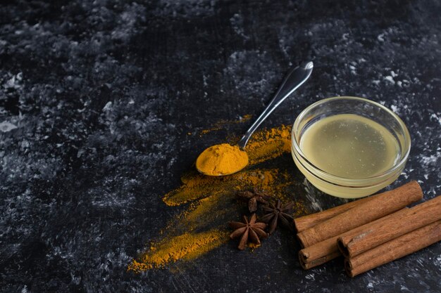 Foto ingredientes para la leche dorada o el latte con cúrcuma polvo de cúrcuma en una cuchara canela pegas de miel en un tazón badian sobre un fondo oscuro