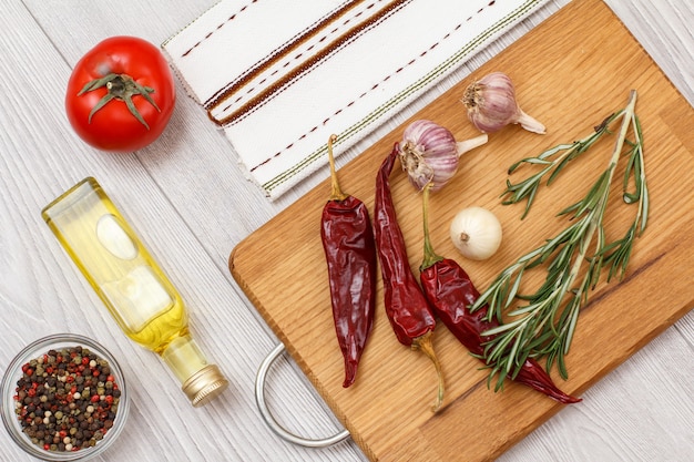 Ingredientes para cozinhar carne ou peixe. Tigela de vidro com pimenta da Jamaica, garrafa de óleo, alho, pimenta, tomate, cebola e alecrim em uma tábua de madeira. Vista do topo.