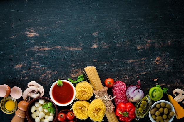 Ingredientes para cozinhar macarrão Macarrão seco Cogumelos salsichas tomates legumes Vista superior Em um fundo preto de madeira Espaço para cópia grátis