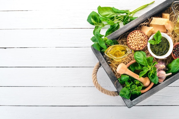 Ingredientes para cozinhar o molho pesto em uma caixa de madeira. Manjericão, queijo parmesão, azeite, pinhões, pimenta, alho. Vista do topo.