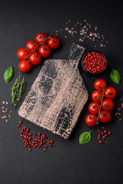 Ingredientes para cozinhar tomates cereja, especiarias salgadas e ervas sobre um fundo escuro de concreto
