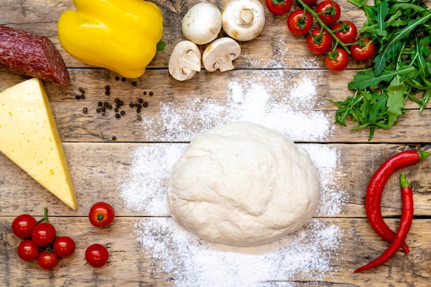 Ingredientes para fazer pizza, antes de assar, em uma mesa de madeira, vista de cima, receita passo a passo