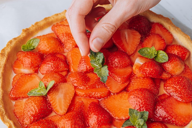 Foto ingredientes para morangos fatiados de torta de morango são colocados em cima da torta e manchados por cima com geleia de limão com folhas de hortelã verde fresca