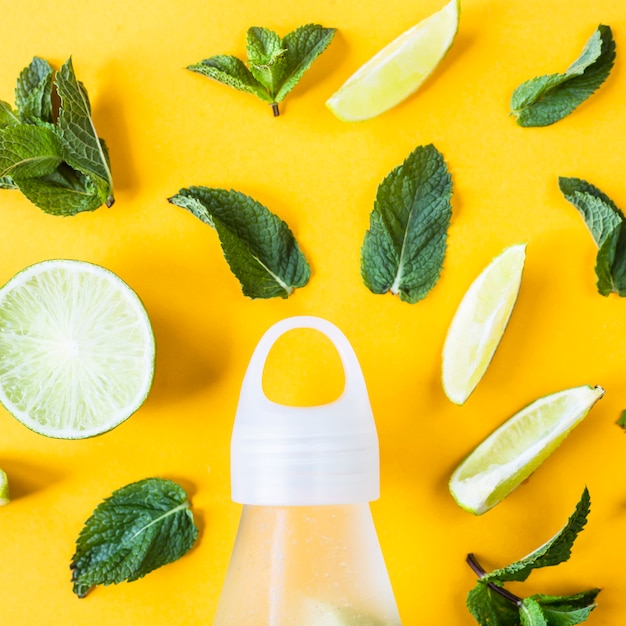 Ingredientes para o mojito de limão e hortelã em um fundo amarelo ao lado de uma garrafa transparente