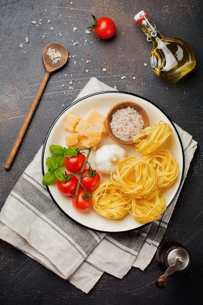 Ingredientes para o prato de massa tradicional italiana. Bolonheses de tagliatelle crus crus, queijo parmesão, azeite, alho, folhas de manjericão, pimenta, tomate cereja. Vista do topo