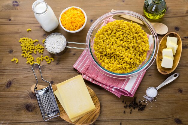 Ingredientes para preparar macarrão com queijo em uma mesa de madeira.