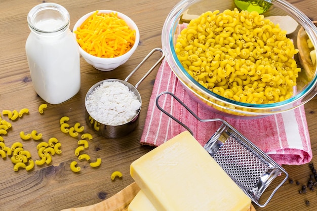 Ingredientes para preparar macarrão com queijo em uma mesa de madeira.