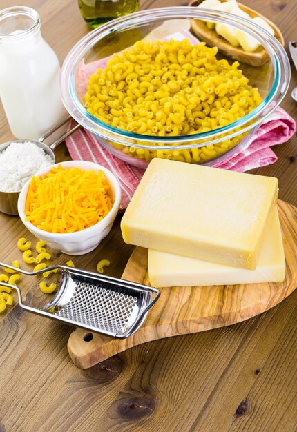 Ingredientes para preparar macarrão com queijo em uma mesa de madeira.