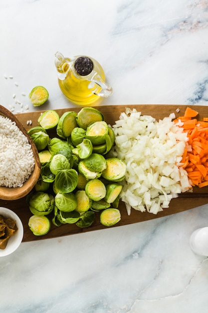 Foto ingredientes para risoto com couve de bruxelas sobre uma tábua de madeira e mesa de mármore