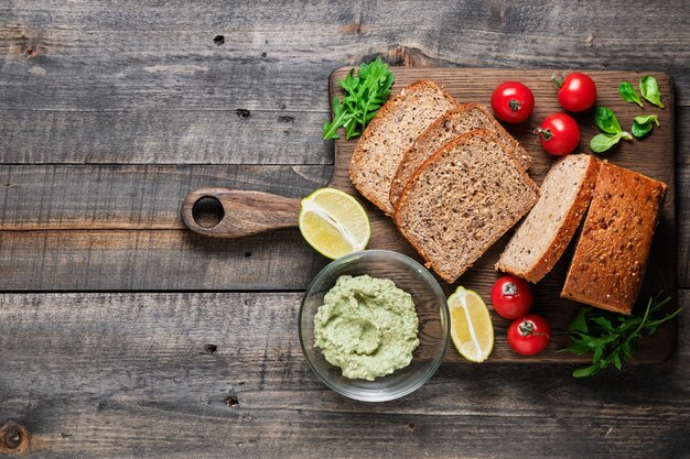 Ingredientes para sanduíches saudáveis. Pão integral caseiro fatiado, tomate cereja, salada de milho, rúcula e guacamole de abacate.