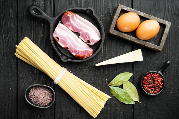 Ingredientes para pasta carbonara. conjunto de comida tradicional italiana, sobre mesa de madera negra, vista superior plana