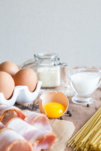 Ingredientes para Pasta Carbonara con tocino, queso, crema y yema en mesa de madera