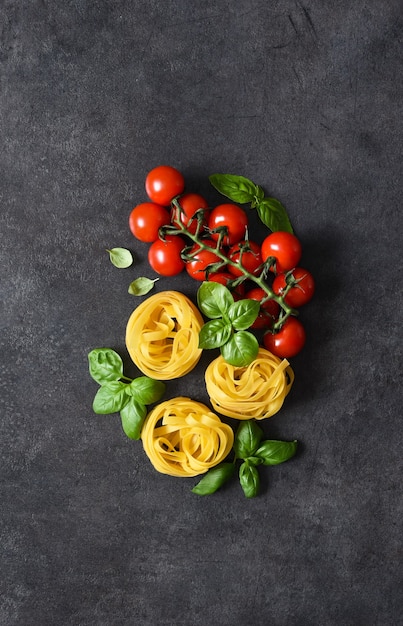 Ingredientes para la pasta. Pasta de tallarines, tomates y albahaca sobre una superficie de hormigón negro.