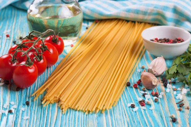 Ingredientes de pasta, toalla a cuadros azul y especias sobre superficie de madera azul.