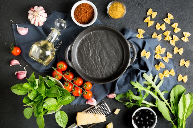 Ingredientes de pasta. Tomates cherry, pasta farfalle, ajo, albahaca, parmesano, espinacas, rúcula, especias y aceite de oliva sobre un fondo oscuro