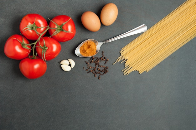 Ingredientes de pasta. tomates, pasta de espagueti, ajo y tomates sobre fondo oscuro grunge. orientado horizontalmente. vista superior