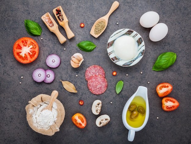 Los ingredientes para la pizza hecha en casa con los ingredientes en fondo oscuro de la piedra con endecha plana.