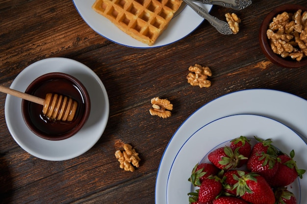 Ingredientes para preparar un desayuno con gofres con miel de fresas y nueces en un plato.