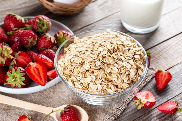 Ingredientes saludables para el desayuno. Granola casera en recipiente de vidrio abierto, leche o yogur, fresas en la mesa de madera - concepto de salud y dieta