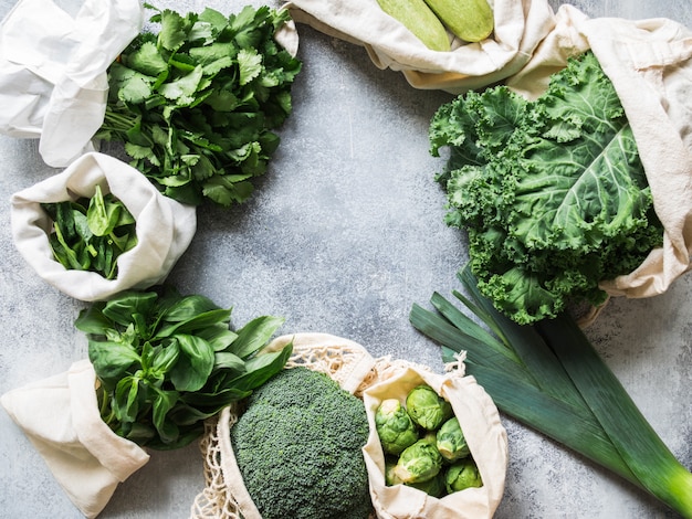 Ingredientes saludables veganos verdes para cocinar. Varios vegetales verdes limpios y hierbas en bolsas textiles. Productos del mercado sin plástico. Concepto de cero desperdicio plano.