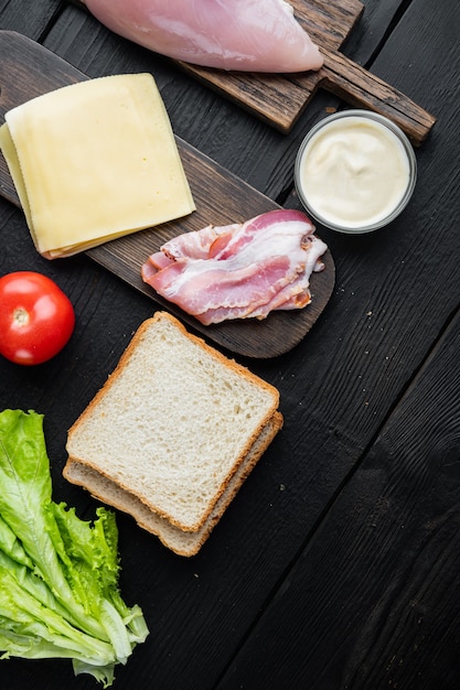 Ingredientes del sándwich club, en la mesa de madera negra, vista superior con espacio para copiar texto