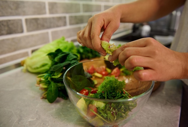 Ingredientes saudáveis para salada crua vegana. Alimentos e conceito de veganismo, vigor e alimentação saudável. Close-up das mãos do chef feminino preparando salada crua de vegan na cozinha de casa.