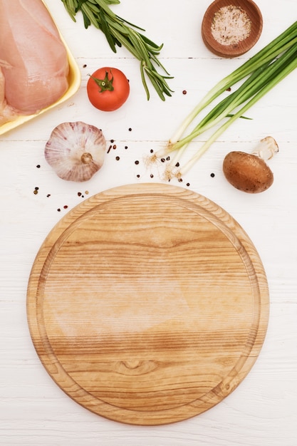 Ingredientes y tabla de cortar redonda. filete de pollo, tomate, cebolla verde, champiñones, ajo, romero. vista desde arriba.