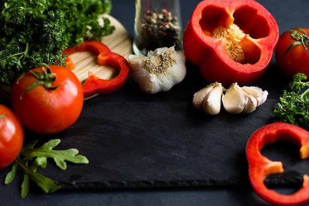 Ingredientes vegetales frescos con especias. Pimientos rojos, tomates, ajo, perejil, rúcula. Sobre un fondo gris.