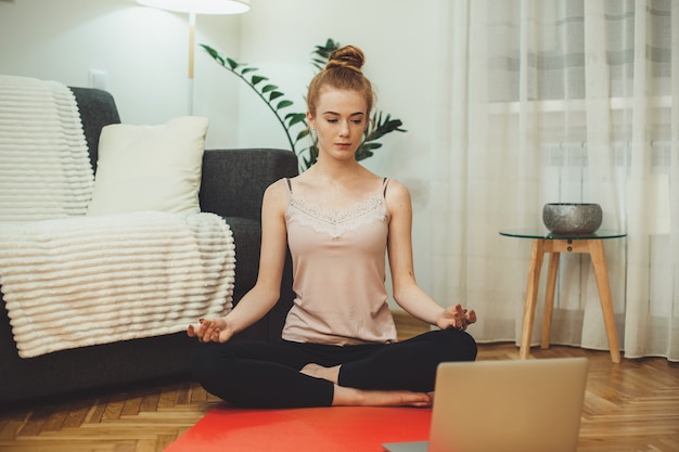 Ingwer kaukasisches Mädchen mit Sommersprossen hat einige Online-Yoga-Lektionen auf dem Boden mit einem Laptop trainieren