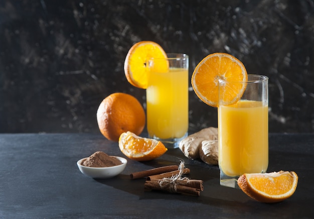 Ingwer-Orangen-Getränk in Glasgläsern, Orange, Ingwer und Zimt auf einem schwarzen Hintergrund. Detox. Frischer Saft.