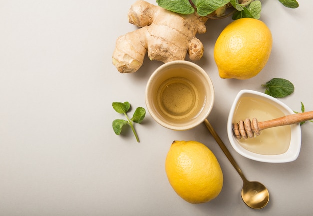 Ingwer-Zitronen-Tee mit Honig. Erwärmender immunstärkender Tee mit Zitrusfrüchten und Ingwer. Tasse, Honig, Ingwerwurzel auf grauem Pastellhintergrund