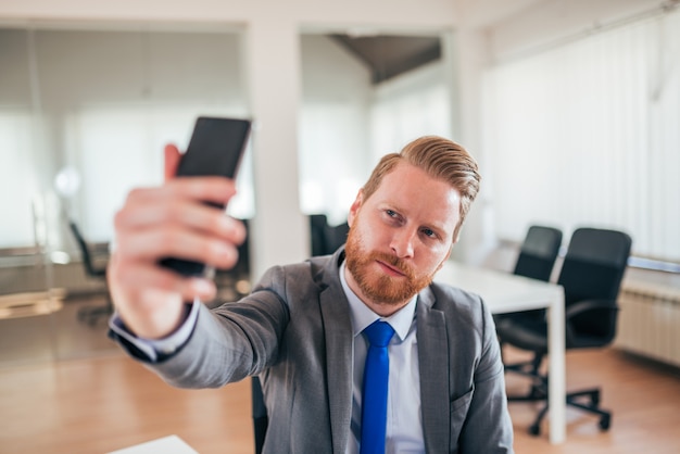 Ingwergeschäftsmann, der selfie im Büro nimmt.