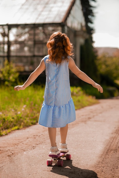 Ingwermädchen in einem blauen Kleid auf einem Skateboard