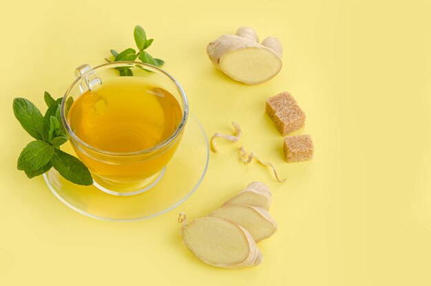 Ingwertee mit Zitrone im Glas Tasse mit braunem Bio-Zucker und Minze auf gelbem Papierhintergrund