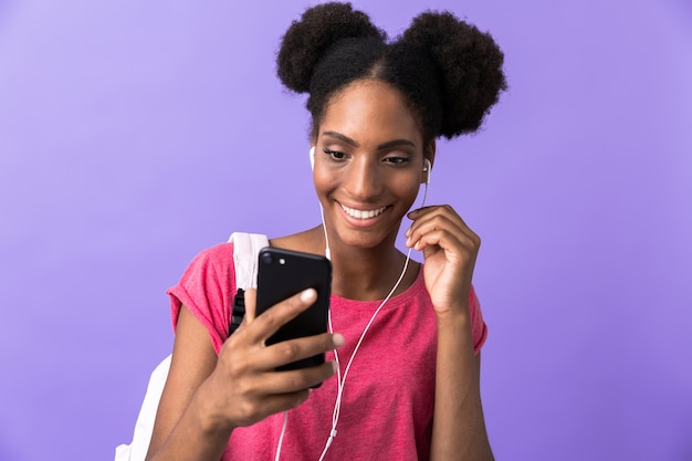 Inhalt Afroamerikaner Studentin mit Rucksack und weißen Kopfhörern mit Smartphone, isoliert