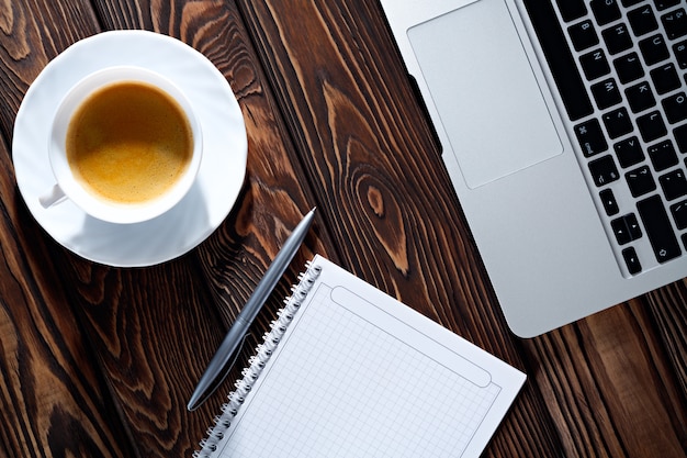 Início da manhã trabalho mesa de escritório com uma xícara de café computador portátil, caderno, caneta. mesa de textura de madeira. Conceito de negócios