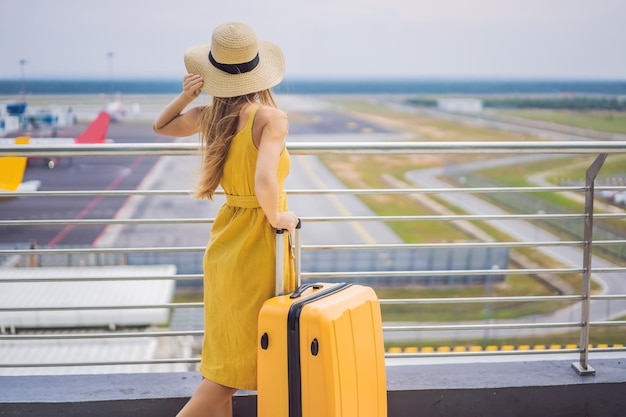 Início de sua jornada Linda jovem viajante em um vestido amarelo e uma mala amarela está esperando seu voo