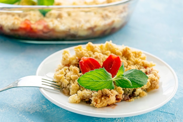 Inicio Ñ ooking. Crumble de ruibarbo o fresa, crujiente sin gluten en una fuente para hornear. Postre de verano en placa sobre fondo azul.