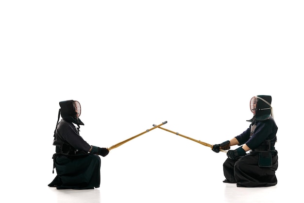 Inicio de la pelea Dos hombres atletas profesionales de kendo en uniforme con casco con espada de bambú shinai contra fondo blanco de estudio