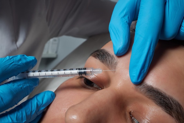 Injeção no salão de spa Mãos de médico em luvas Closeup Paciente do sexo masculino Tratamento de beleza Procedimento de pele saudável Rosto de jovem Rejuvenescimento plasmolifting