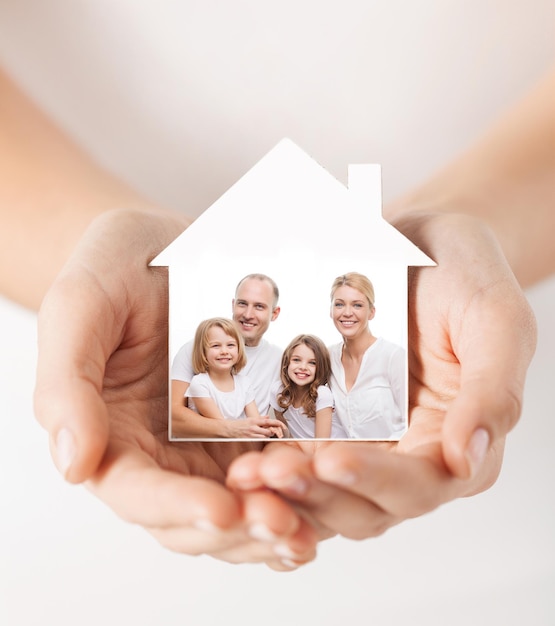 Inmobiliaria, seguro de hogar y concepto de felicidad - cierre de manos femeninas sosteniendo la casa blanca con una foto familiar feliz