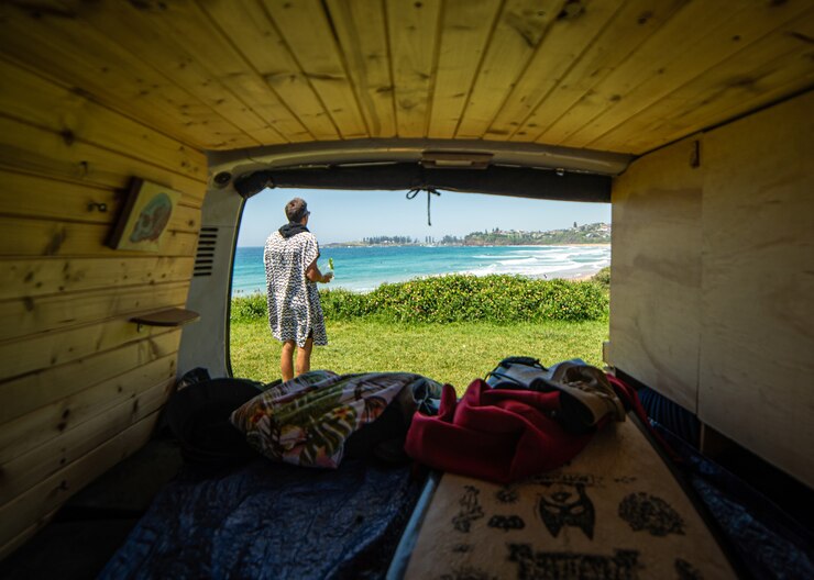 Innenansicht von einem Campervan mit Surfer draußen, der den Strand beobachtet